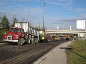 Dump truck and paving crew working on a road beside a highway overpass