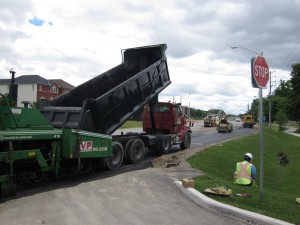 A dump truck feeding an asphalt paver on a suburban municipal street