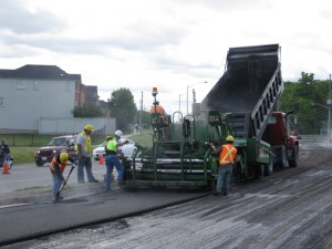 Paving crew working behind a paver and dump truck on an urban road